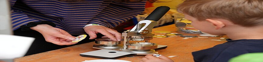 Kind an einer Buttonmaschine