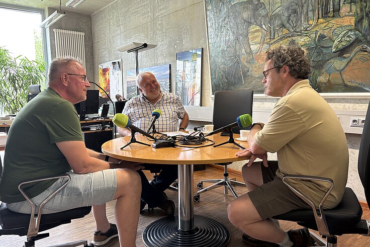 Zoodirektor, Tierpfleger und Moderator sitzen in einem Büro am Tisch und plaudern