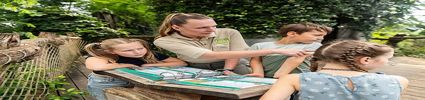 Kinder und Lotsin an einem Ringbuch über die Tiere in Gondwanaland